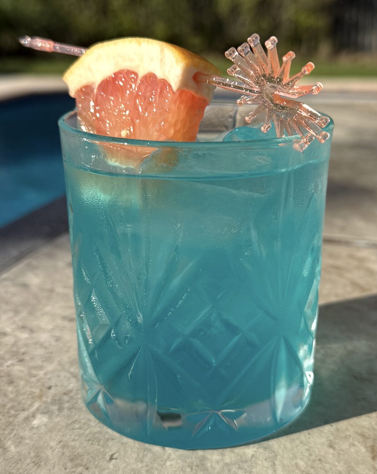 Bright blue signature cocktail with grapefruit garnish by the pool