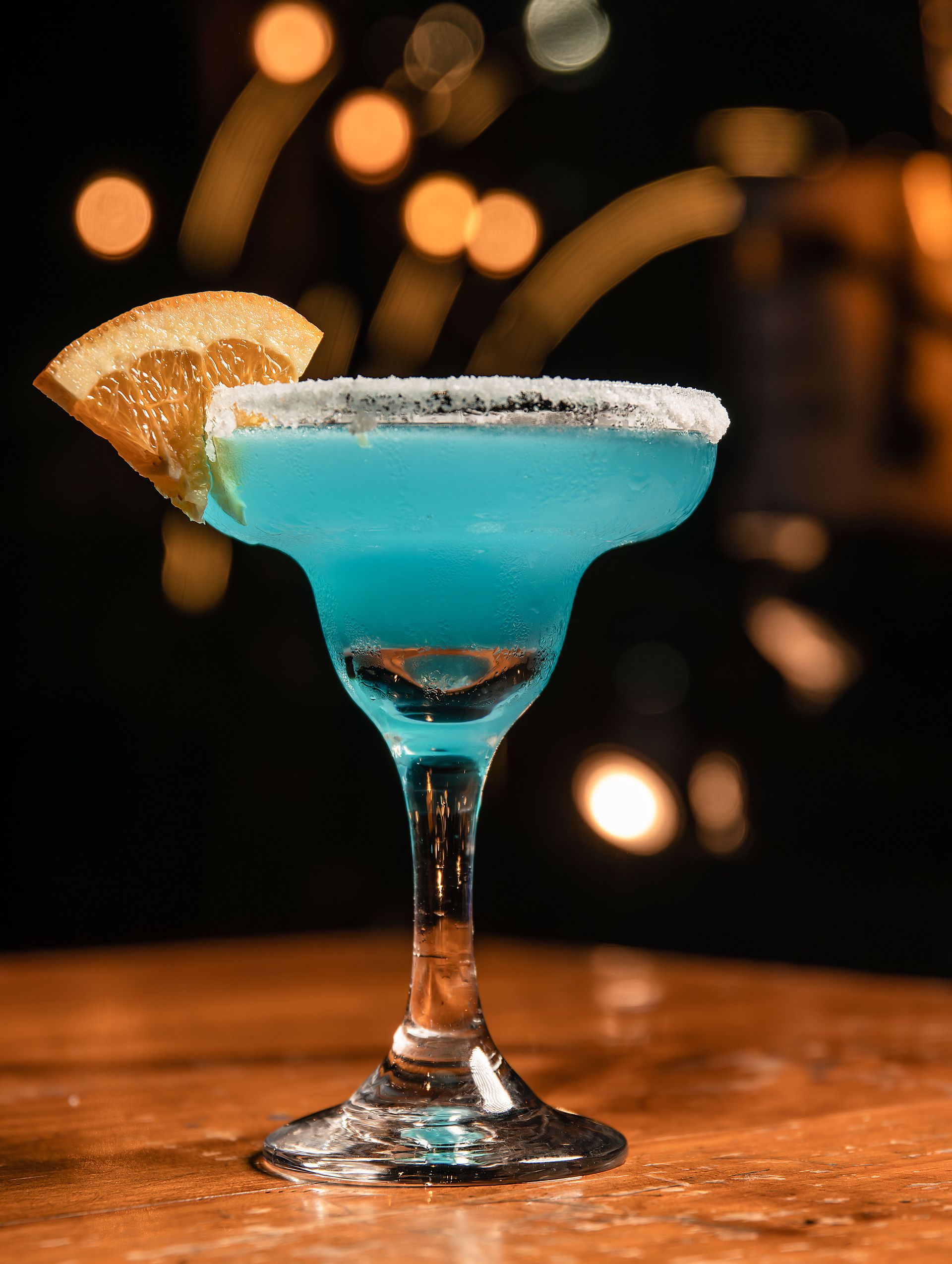 Vivid blue Poolside Blue signature cocktail with a citrus wheel garnish